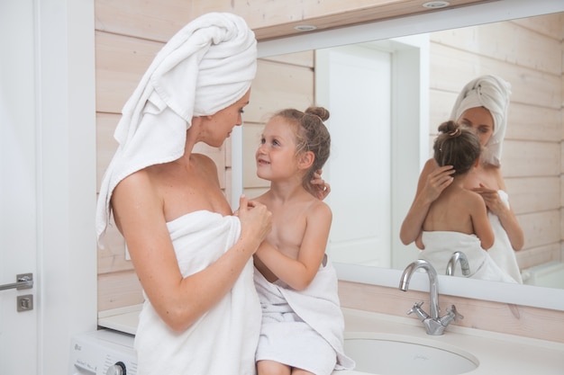 Felice famiglia amorevole madre e figlia con asciugamani trascorrere del tempo insieme in bagno bianco.