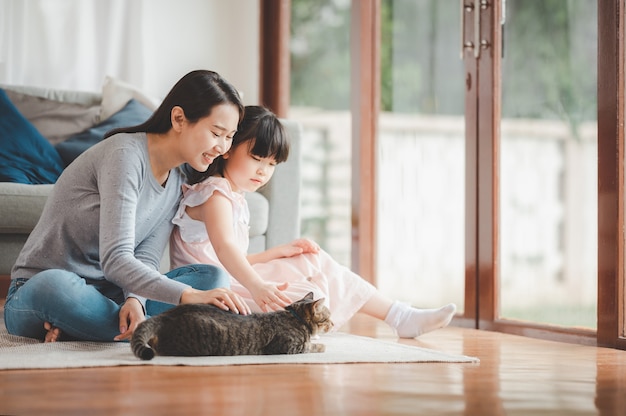 Felice famiglia asiatica madre e figlia che giocano con il gatto a casa in soggiorno. Incentrato sulla madre