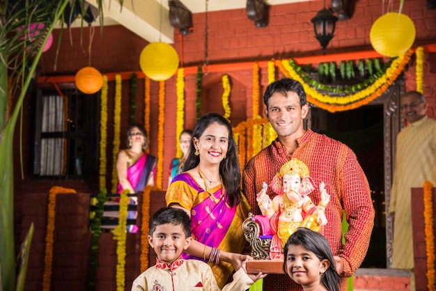 Felice famiglia indiana che celebra il festival di Ganesh o Chaturthi - Accogliere o eseguire Pooja e mangiare dolci in abiti tradizionali a casa decorata con fiori di calendula