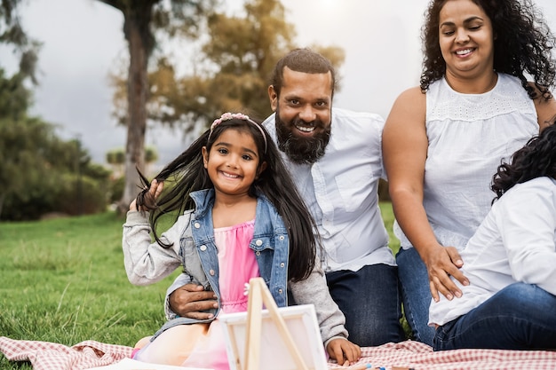 Felice famiglia indiana che si diverte a dipingere con i bambini all'aperto nel parco cittadino - Focus principale sul viso della ragazza