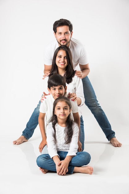 Felice famiglia indiana di 4 persone in piedi isolato su sfondo bianco. Giovane coppia con bambini che indossano jeans blu e top bianco. messa a fuoco selettiva