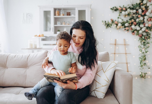 Felice famiglia interrazziale La madre caucasica e suo figlio afroamericano leggono un libro sul divano