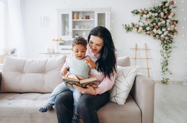 Felice famiglia interrazziale La madre caucasica e suo figlio afroamericano leggono un libro sul divano