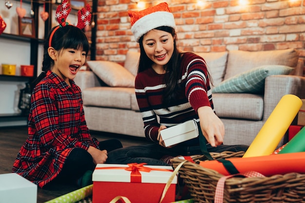 felice famiglia madre e bambino confezione regalo di Natale. santa mamma che punta il dito sulla carta incartata facendo artigianato fatto a mano a casa. adorabile ragazzo che aiuta con il lavoro di squadra artistica al chiuso.