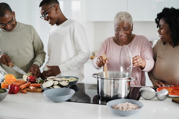 Felice famiglia nera che cucina cibo vegano all'interno della cucina a casa