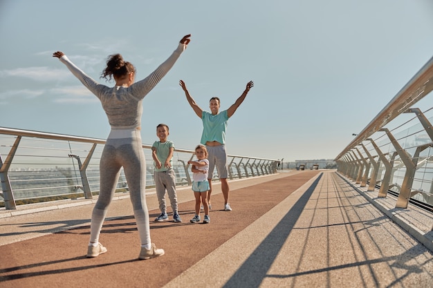 Felice famiglia sana e sportiva stanno facendo allenamenti di allenamento in una giornata di sole
