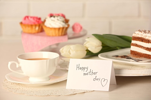 Felice festa della mamma saluto con tulipani tazza di tè e deliziosi cupcakes sul primo piano della tavola di legno