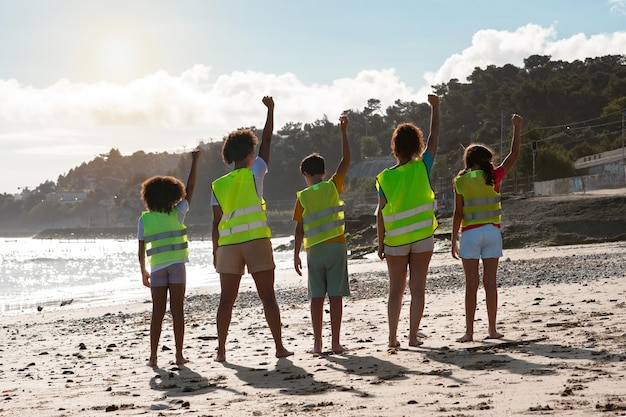 Felice fiducioso diversi bambini adolescenti volontari in giubbotti alzano la mano per celebrare la vittoria sulla spazzatura