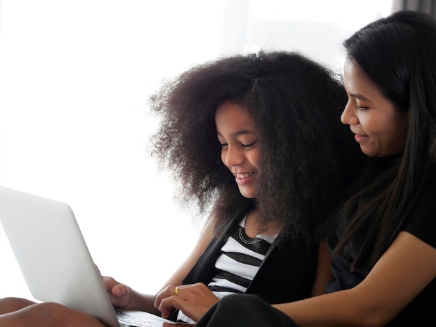 Felice figlia afroamericana e madre asiatica che usano il laptop insieme seduti sul divano a casa