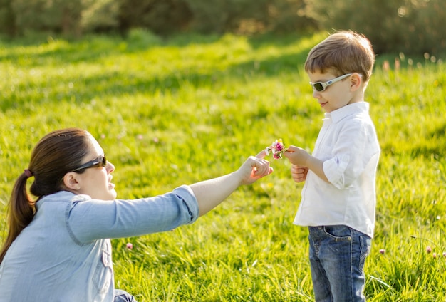 Felice figlio carino che dà un mazzo di fiori a sua madre in un campo soleggiato