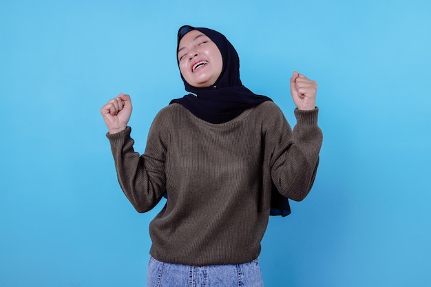 Felice gioiosa donna che indossa l'hijab stringe i pugni e celebra il buon risultato sorride ampiamente essendo in alto spirito fa gesto di trionfo