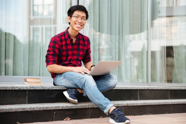Felice giovane asiatico in camicia a quadri con laptop all'aperto
