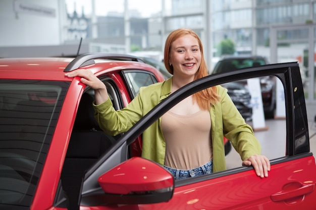 Felice giovane autista femminile che esamina le auto in vendita presso la concessionaria