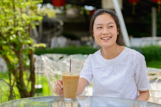 Felice giovane bella donna asiatica pensando presso la caffetteria all'aperto