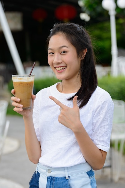 Felice giovane bella donna asiatica tenendo il caffè presso la caffetteria all'aperto