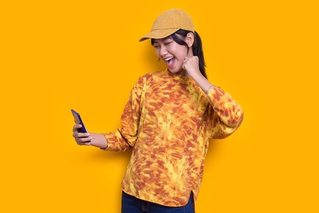 felice giovane bella donna asiatica utilizzando il telefono cellulare isolato su sfondo giallo