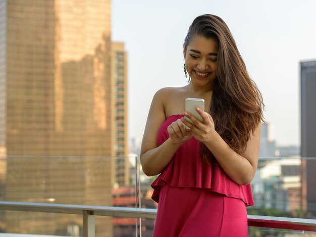 Felice giovane bella donna indiana utilizzando il telefono contro la vista della città