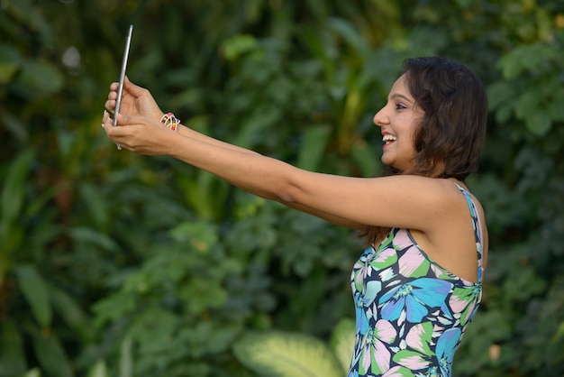 Felice giovane bella donna indiana videochiamata con tavoletta digitale al parco