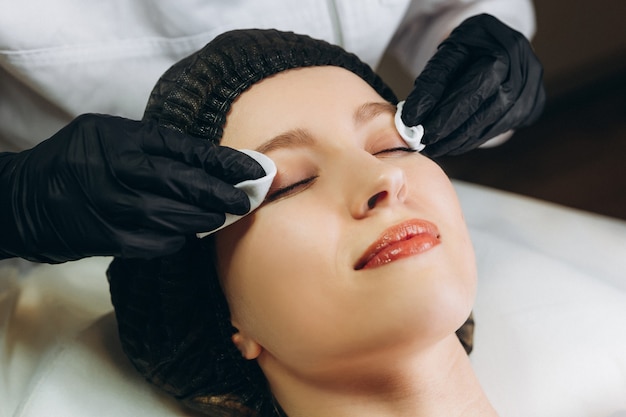 Felice giovane bella donna sorridente con gioia mentre estetista professionista pulisce il viso