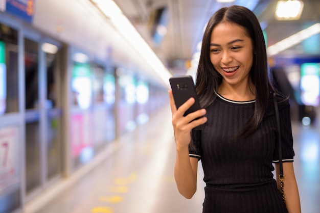 Felice giovane bella donna turistica asiatica utilizzando il telefono alla stazione della metropolitana