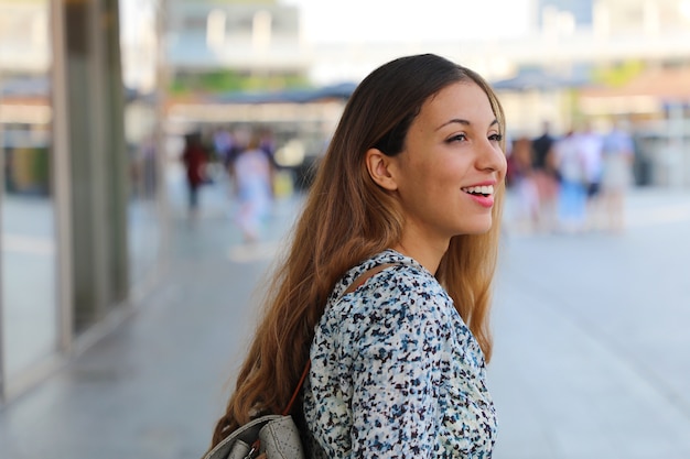 Felice giovane bella donna urbana guardando al lato con sfondo sfocato della città