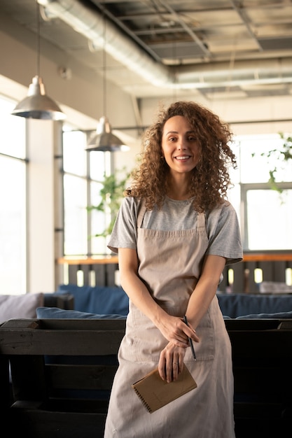 Felice giovane cameriera sorridente con lunghi capelli ondulati scuri ti guarda