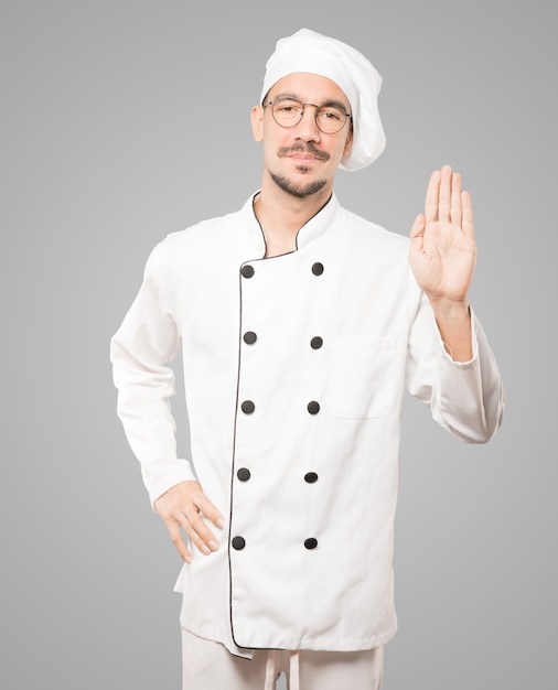 Felice giovane chef facendo un gesto di arresto con il palmo della mano