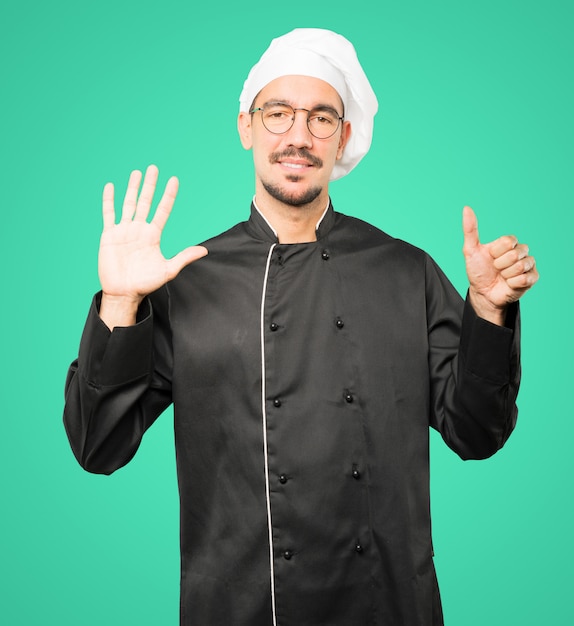 Felice giovane chef facendo un gesto numero sei con le mani