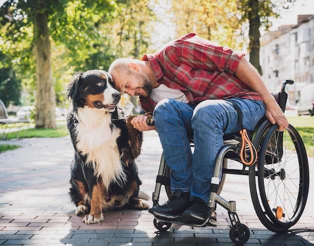 Felice giovane con disabilità fisica su una sedia a rotelle con il suo cane