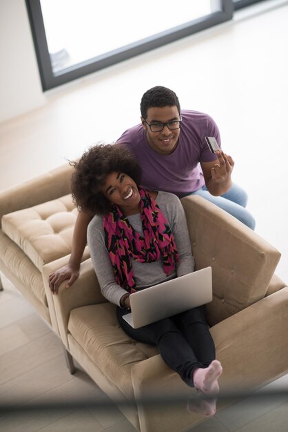 Felice giovane coppia afroamericana che fa shopping online tramite il computer portatile utilizzando la carta di credito a casa