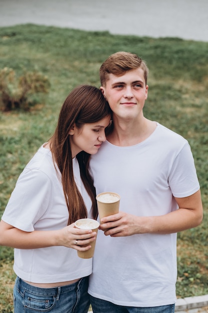 Felice giovane coppia cammina per le strade della città e beve il caffè da una tazza di cartone.