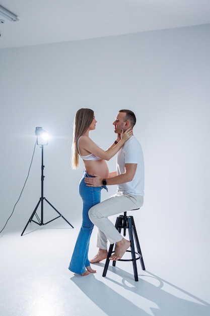 Felice giovane coppia che aspetta un bambino in magliette bianche e jeans su sfondo bianco felicità della gravidanza e del parto Una felice coppia sposata aspetta un bambino