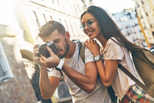 Felice giovane coppia che fotografa qualcosa e sorride mentre sta in piedi all'aperto