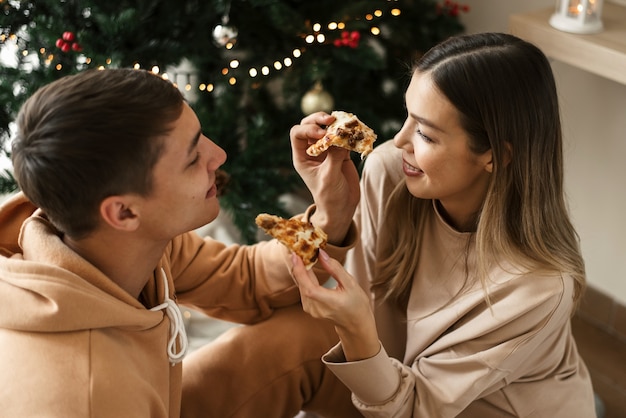 Felice giovane coppia che mangia pizza a casa vicino all'albero di Natale