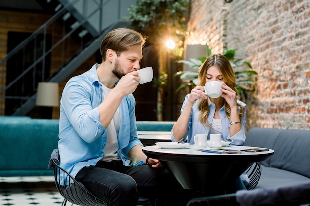 Felice giovane coppia con passaporti e biglietti, seduto al tavolo e bere caffè, prima del viaggio. Caffetteria nella hall dell'hotel, sala d'aspetto