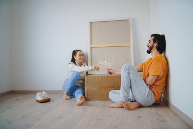 Felice giovane coppia con scatole e vino che si spostano in un nuovo appartamento, una nuova casa e un concetto di trasferimento.