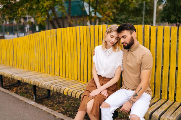 Felice giovane coppia di turisti che riposano nel parco cittadino seduti abbracciati con gli occhi chiusi sulla panchina in una giornata estiva godendosi il tempo trascorso insieme
