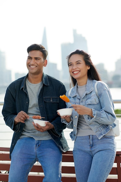 Felice giovane coppia in piedi sul ponte godendo città vide e mangiare gustoso cibo di strada