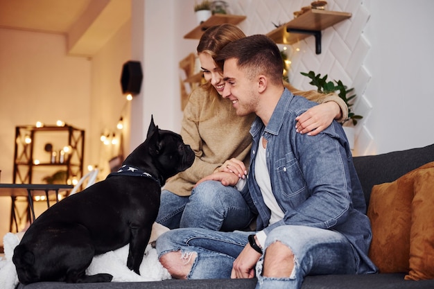 Felice giovane coppia moderna seduta sul divano di casa con il loro simpatico cane.