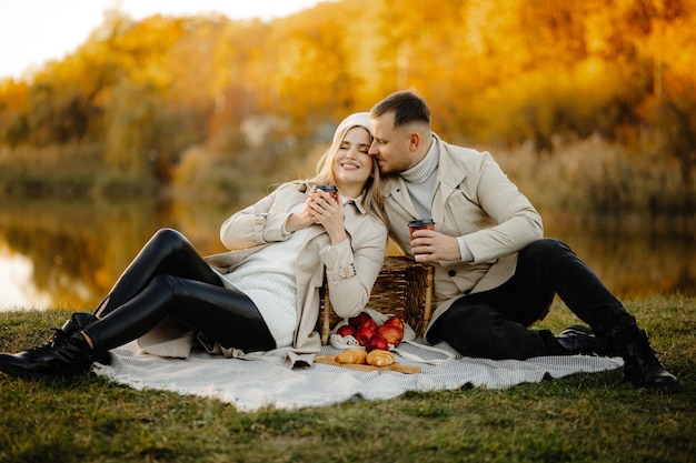 Felice giovane coppia picnic all'aperto in una soleggiata giornata autunnale, coppia seduta sull'erba nel parco autunnale