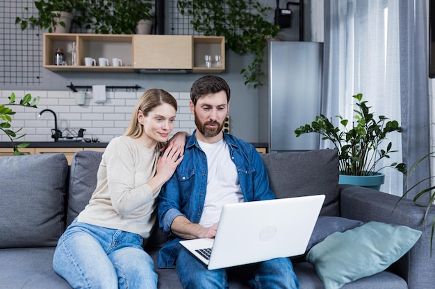 Felice giovane coppia sposata uomo e donna insieme a casa seduto sul divano sorridente e utilizzando il computer portatile