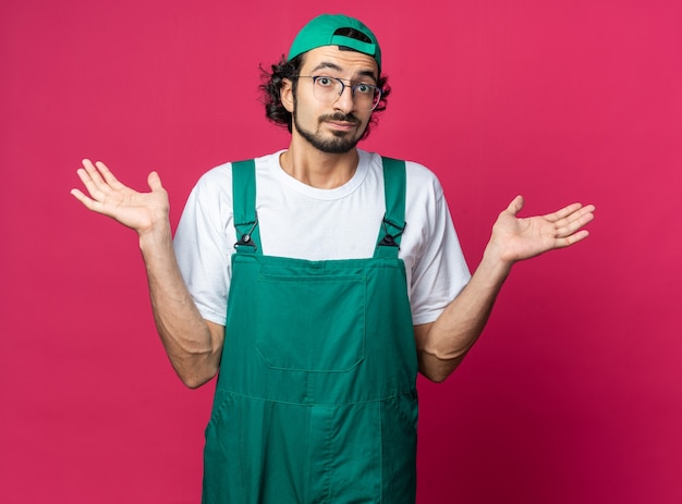 Felice giovane costruttore che indossa l'uniforme con il berretto che allarga le mani