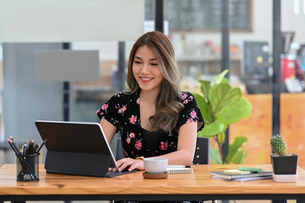 Felice giovane donna asiatica che lavora online con il tablet del computer seduto nella caffetteria