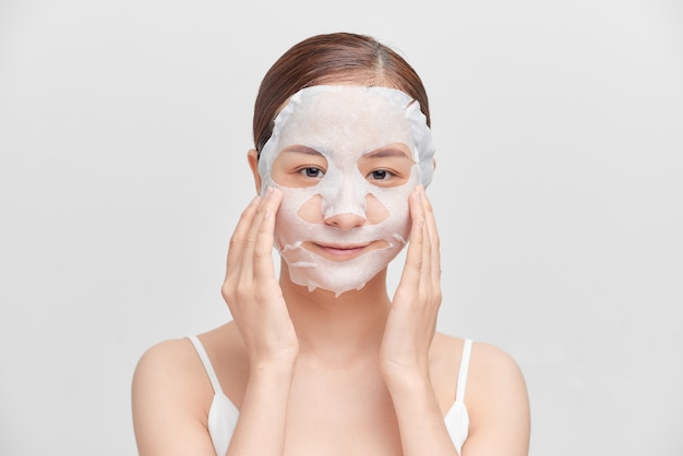 Felice giovane donna asiatica con maschera cosmetica isolato su sfondo bianco.