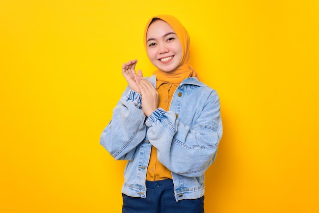 Felice giovane donna asiatica in giacca di jeans che sembra sicura di sé con la faccia sorridente isolata su sfondo giallo
