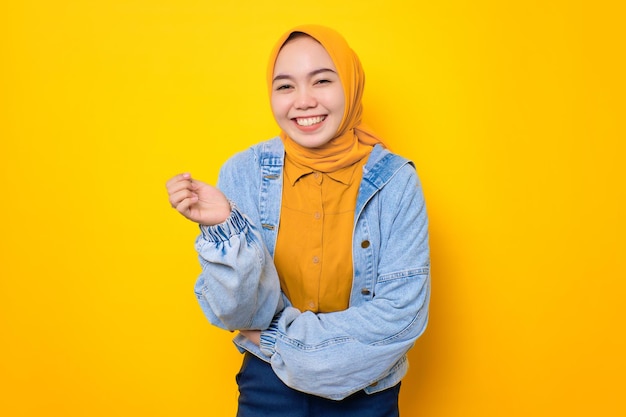 Felice giovane donna asiatica in giacca di jeans sorridente soddisfatto e guardando fiducioso isolato su sfondo giallo