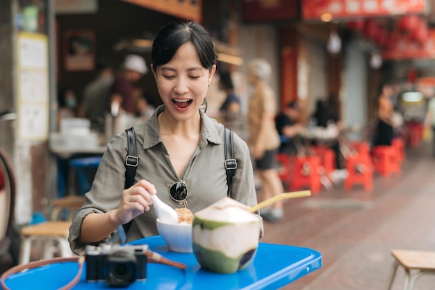 Felice giovane donna asiatica viaggiatore con zaino che si gode il cibo di strada al mercato alimentare di strada della città cinese a Bangkok Tailandia Viaggiatore che controlla le strade laterali