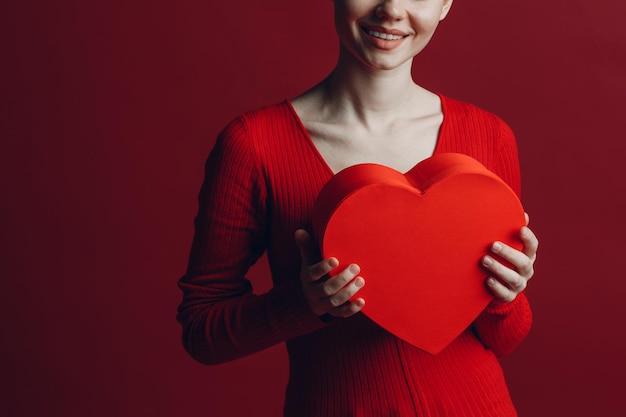 Felice giovane donna azienda scatola a forma di cuore nel giorno di San Valentino a sfondo rosso