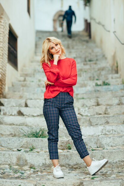 Felice giovane donna bionda in piedi su bellissimi passi in strada.