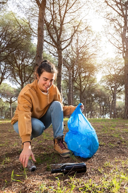 Felice giovane donna caucasica che raccoglie la foresta di pulizia delle bottiglie di plastica. Copia spazio. Immagine verticale. Concetto di ecologia.